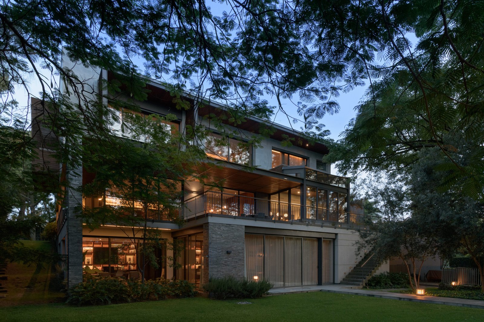 Casa PSC iluminada entre el jardín al anochecer